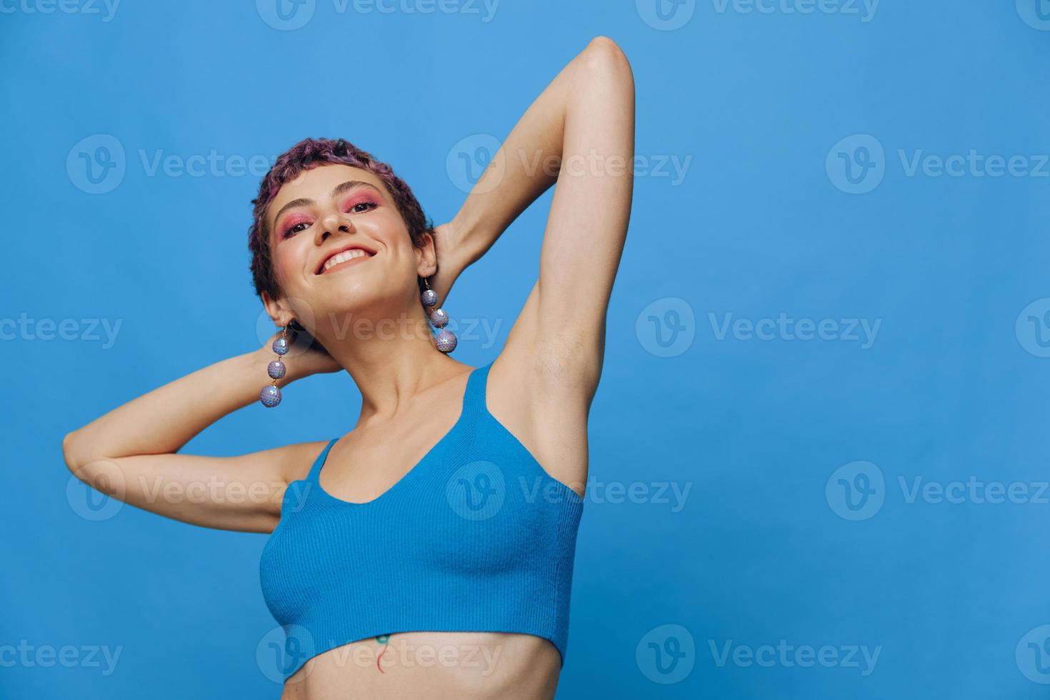 giovane atletico moda donna con colorato capelli e corto taglio di capelli in posa e danza nel blu abbigliamento sportivo sorridente e guardare a il telecamera su un' blu monocromatico sfondo foto