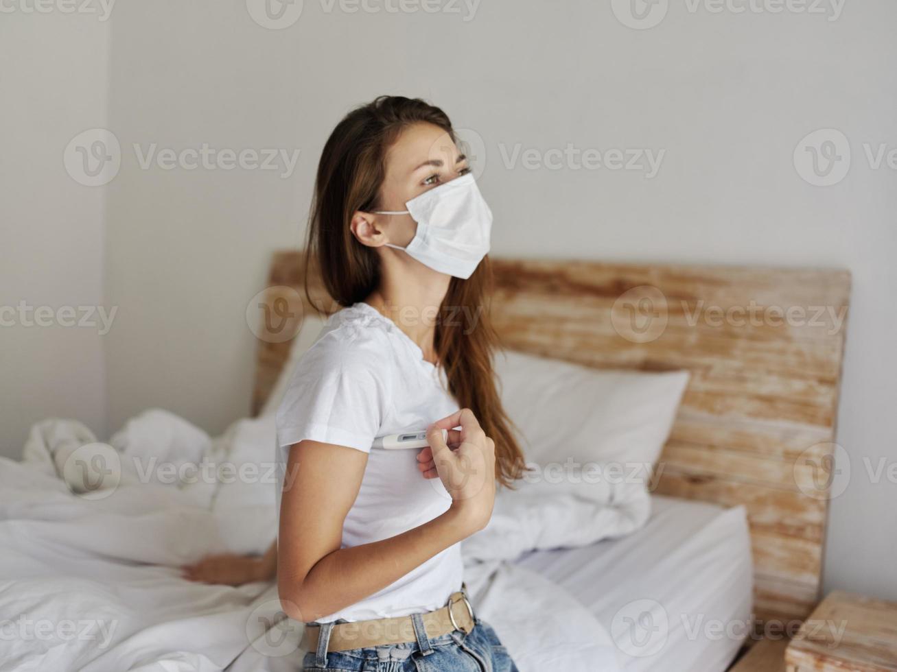 donna nel medico maschera con un' termometro sotto sua braccio e seduta su  il letto Salute dai un'occhiata 22642740 Stock Photo su Vecteezy