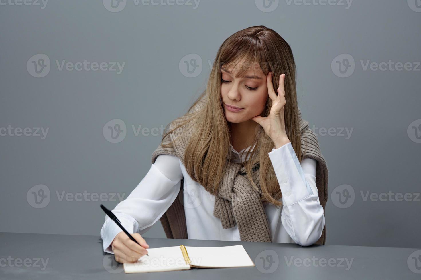 triste stanco giovane bionda alunno signora libero professionista nel caldo maglione fare compiti a casa seduta a posto di lavoro nel grigio moderno casa ufficio. a distanza lavoro, formazione scolastica e carriera professione concetto. copia spazio foto