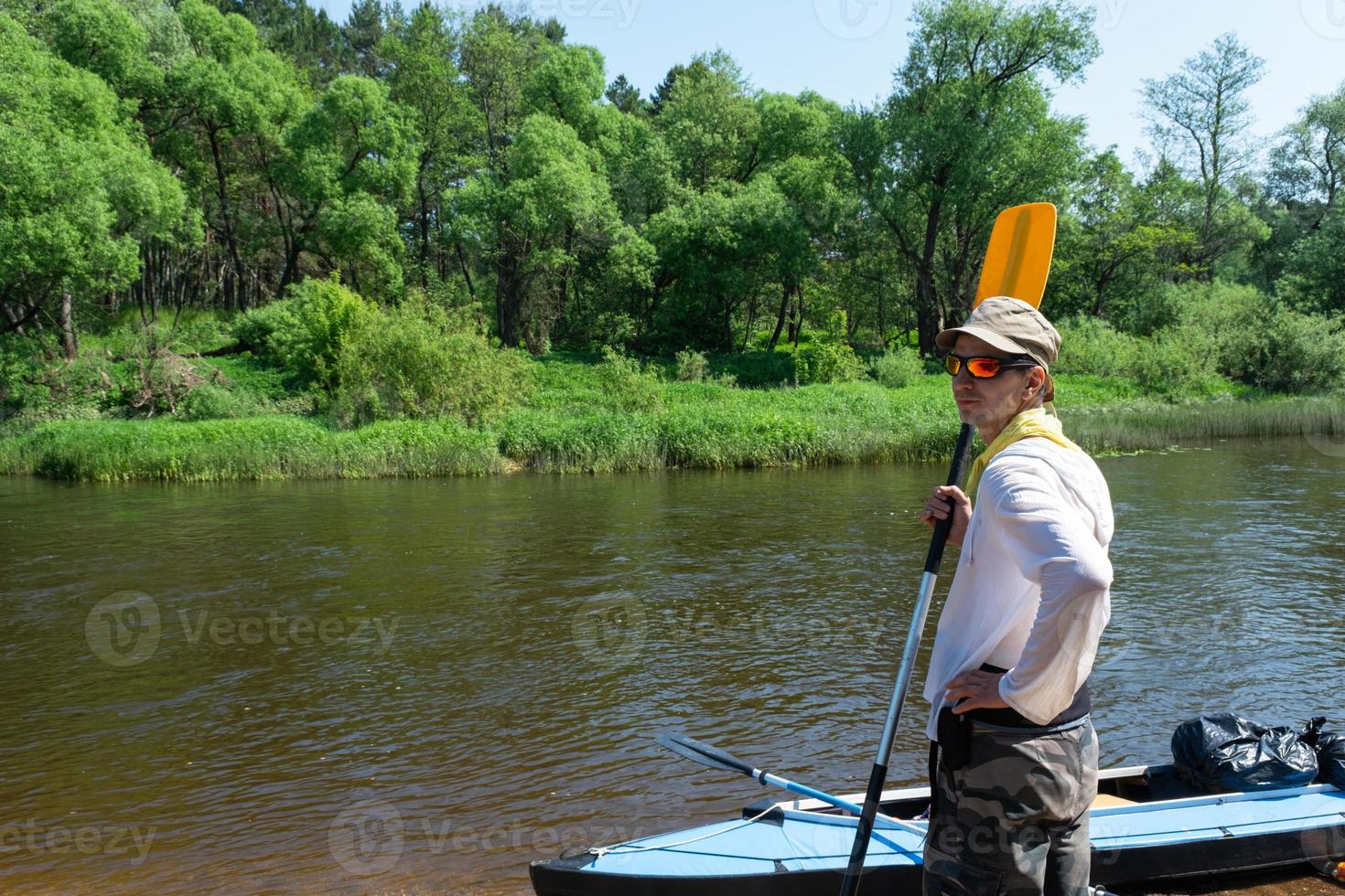 un' uomo con un' kayak pagaia per rafting sta su il fiume banca. sport acqua escursione, un' estate avventura. eco-friendly e estremo turismo, attivo e salutare stile di vita foto