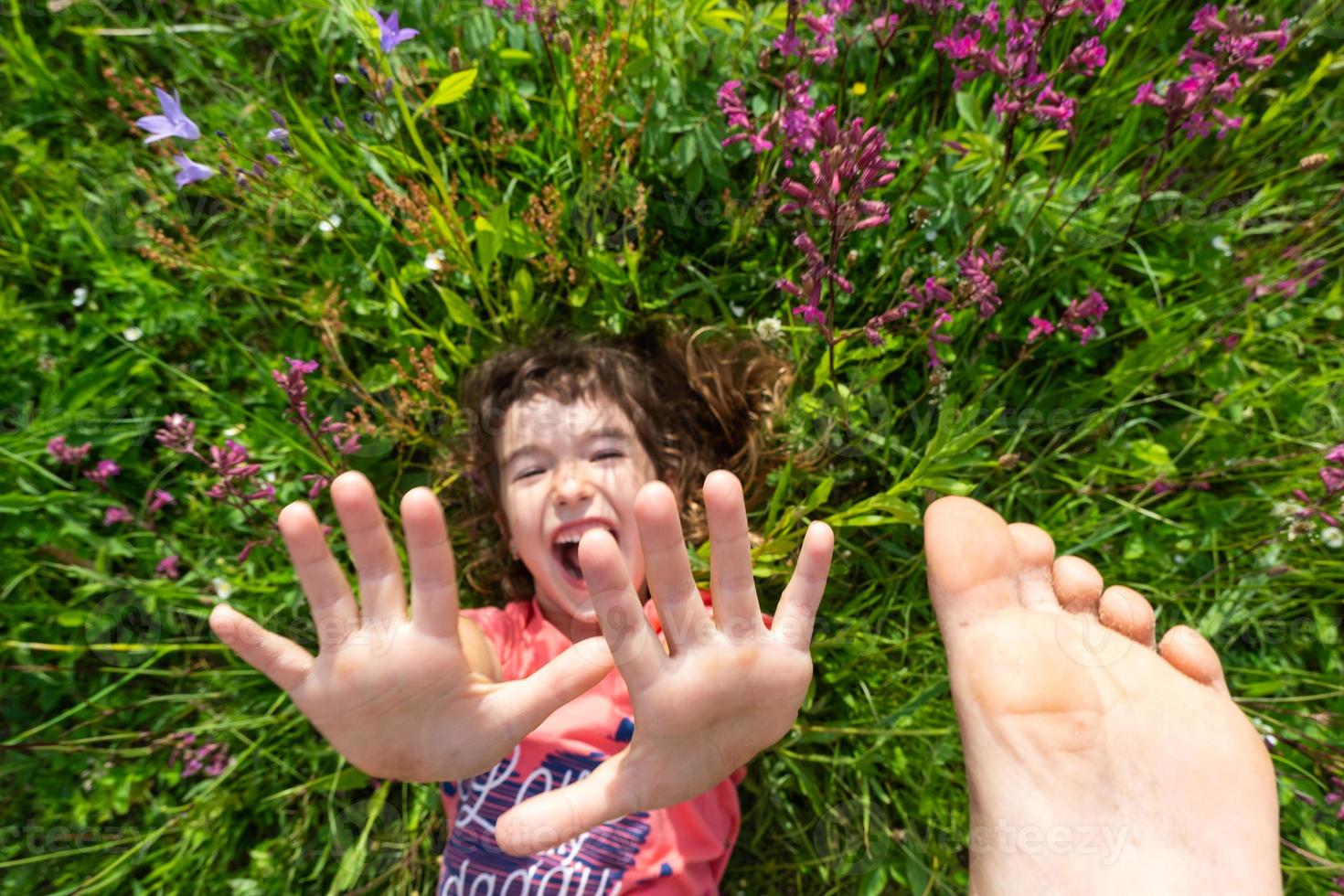 ritratto di un' bambino ragazza nel estate dire bugie nel il erba e fiori selvatici con tacchi e palme. estate volta, la libertà foto