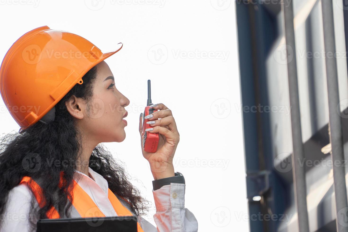 ritratto di femmina lavoratore nel carico contenitori nel spedizione contenitore cortile. donna Tenere Ricetrasmittente e digitale tavoletta. foto