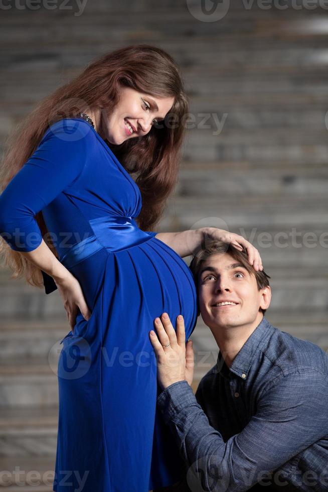 bello uomo ascolta per pancia di il suo bellissimo incinta moglie e sorrisi foto