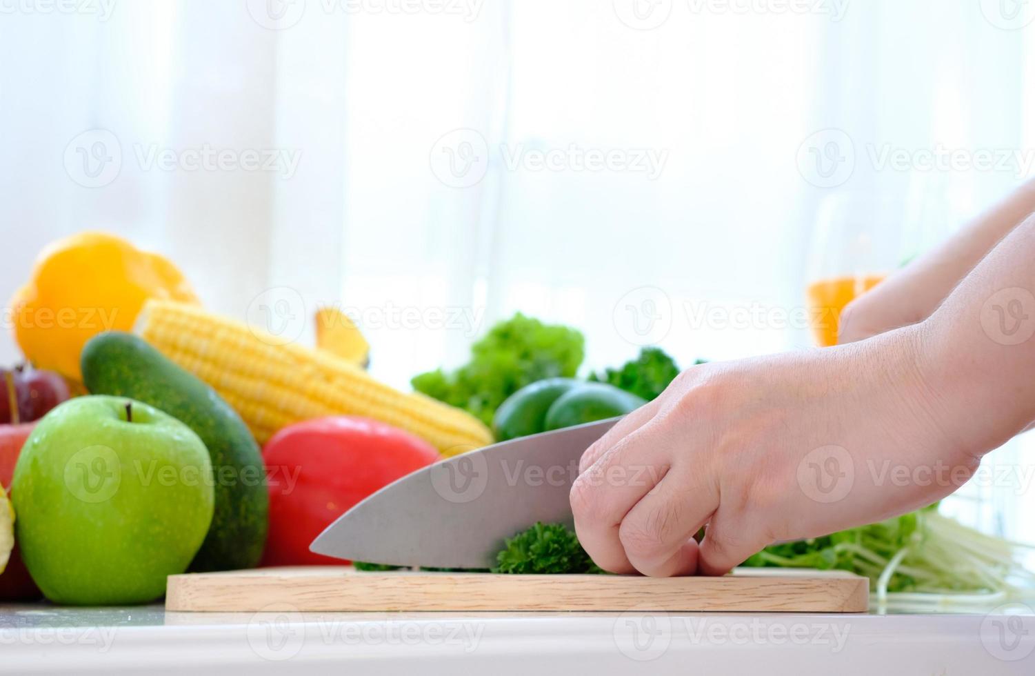 mani usando un coltello per tagliare le verdure su un tagliere di legno foto