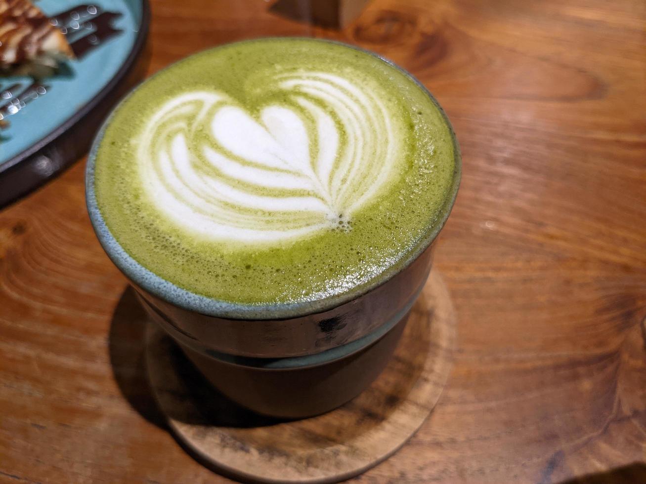 vicino su verde matcha latte macchiato al di sopra di il di legno tavolo su il bar e resto. il foto è adatto per uso per caffè negozio sfondo, menù manifesto e matcha soddisfare media.