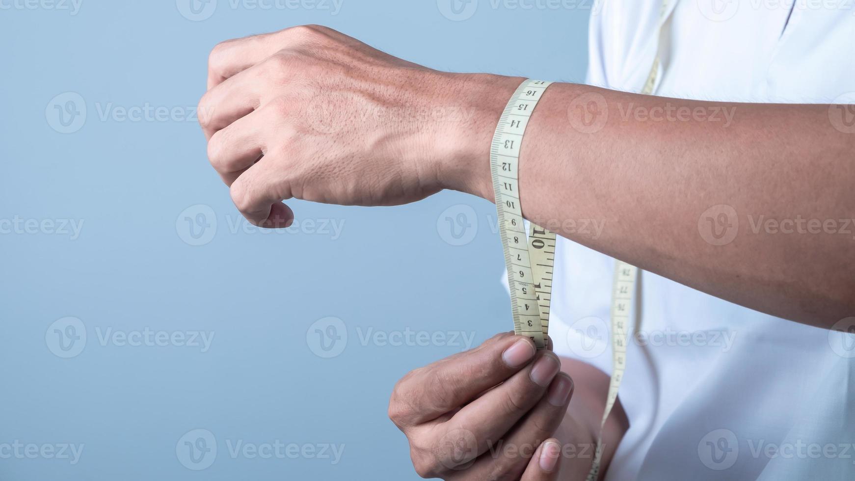 un' uomo le misure il suo polso con un' nastro misurare su leggero blu sfondo, peso perdita concetto foto