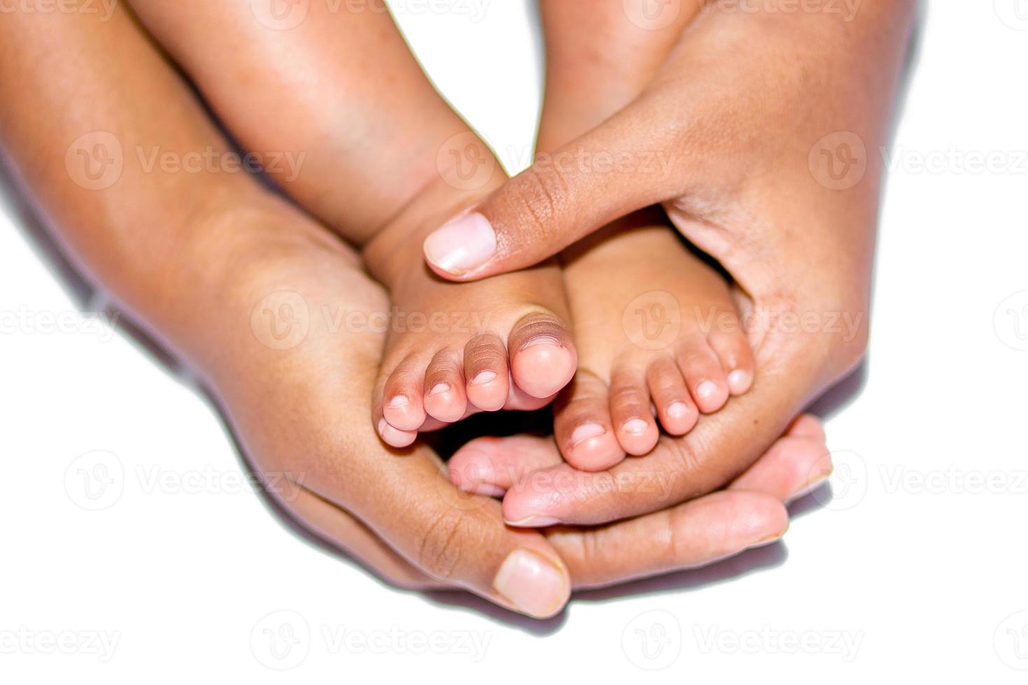 il morbido gambe di un' bambino posto su il palma di il La madre di Due mani su un' bianca sfondo. foto