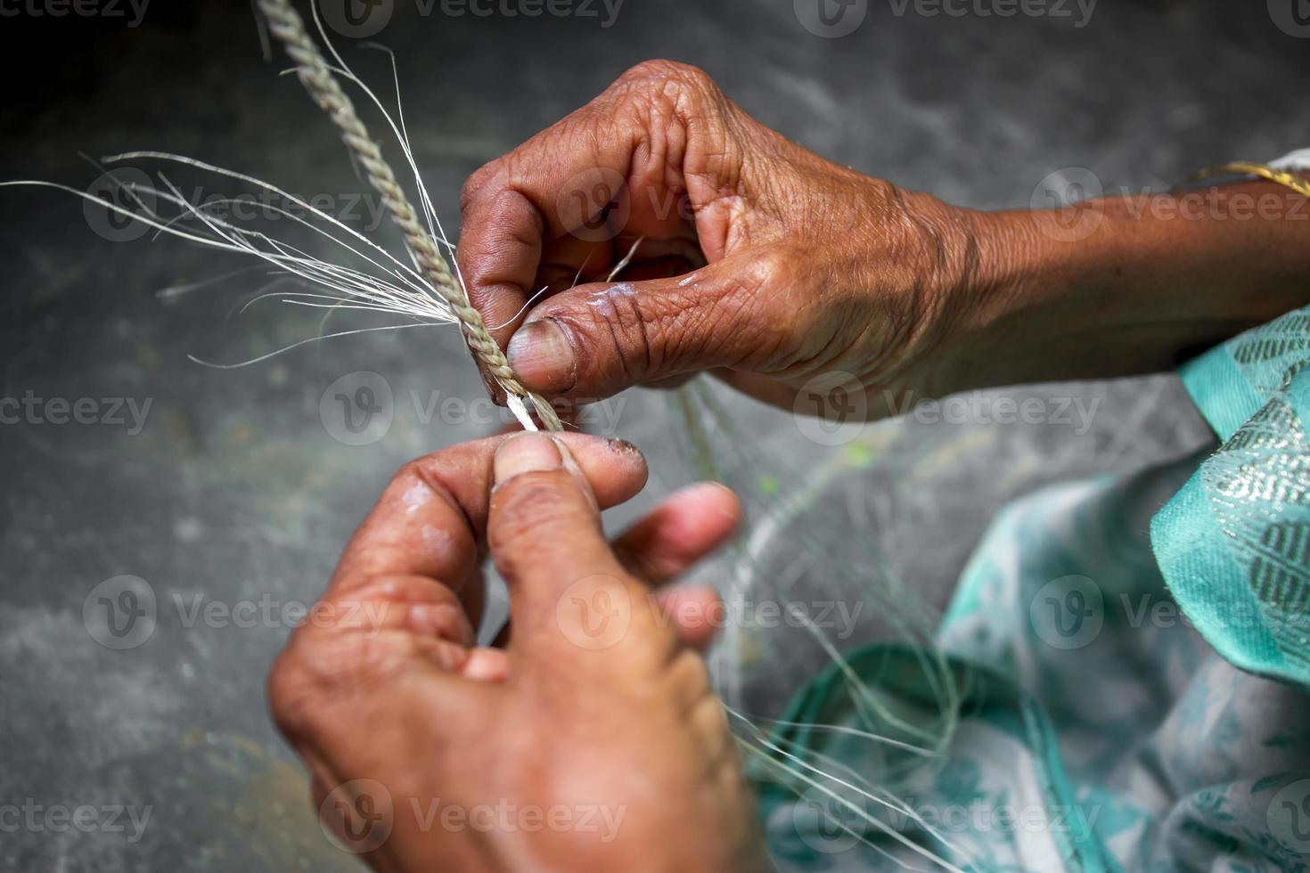 un vecchio età donna è fabbricazione su il suo magro mani un' corda a partire dal il Banana albero fibra a madhupur, tanga, bangladesh. foto
