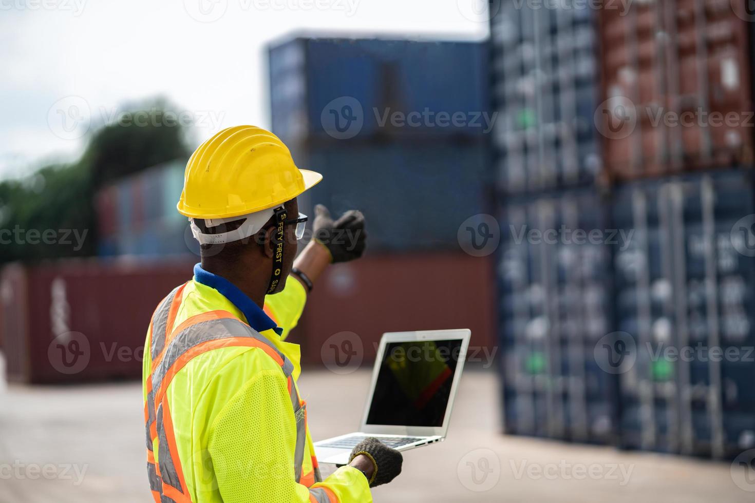 ingegnere uomo lavoratore nel protettivo sicurezza tuta uniforme con giallo elmetto protettivo e uso il computer portatile dai un'occhiata contenitore a carico spedizione magazzino. mezzi di trasporto importare, esportare logistica industriale servic foto