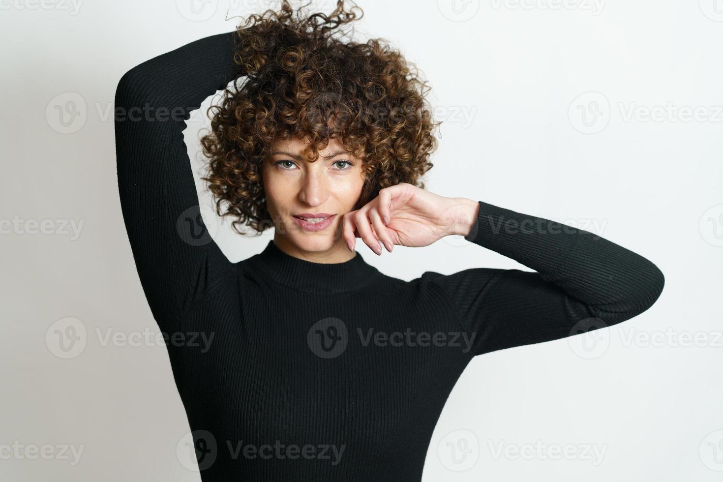 contento femmina con Riccio capelli sorridente con mani vicino sua testa foto