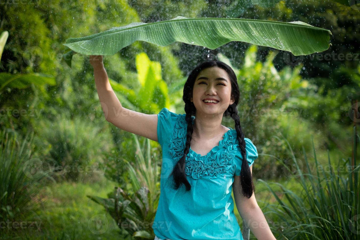 donna asiatica con i capelli neri che tiene una foglia di banana sotto la pioggia foto
