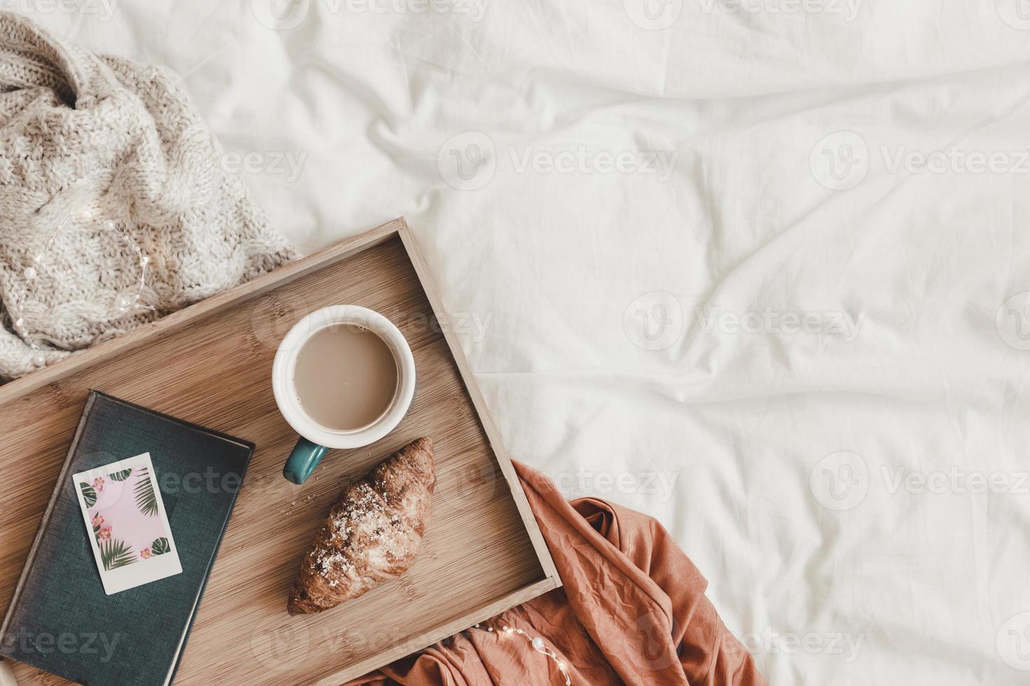 croissant e caffè vicino al libro sul letto, vista dall'alto foto