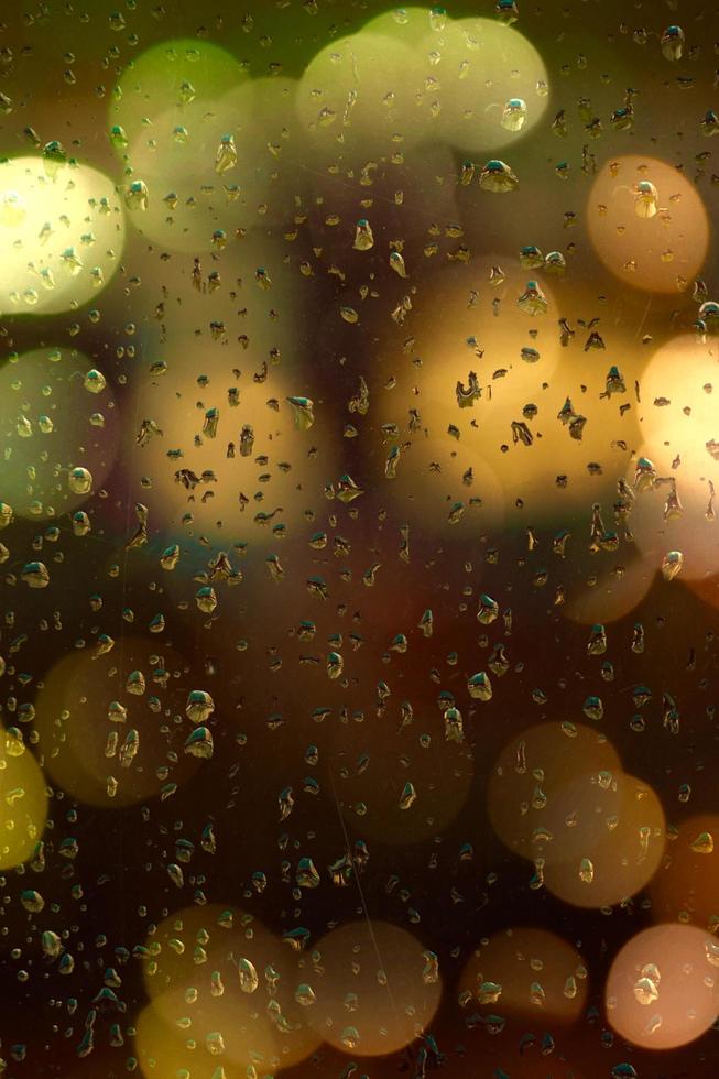 gocce di pioggia e luci bokeh sulla finestra foto