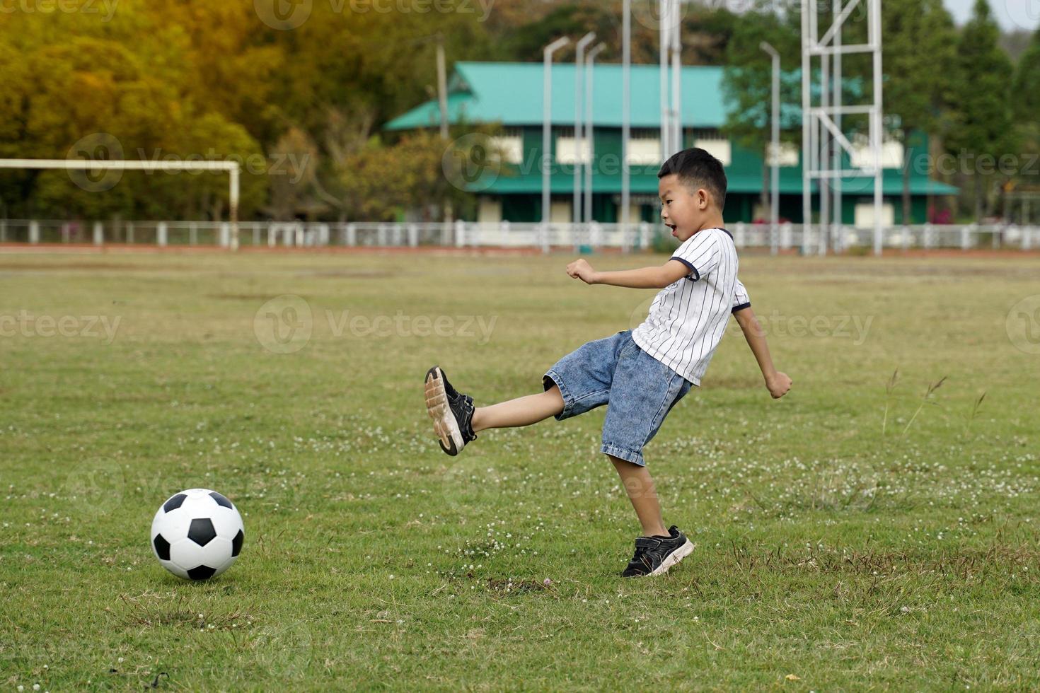 asiatico ragazzo calciando palla nel calcio campo. concetto. all'aperto attività, sport, terreno di gioco, tempo libero attività. morbido e selettivo messa a fuoco. foto