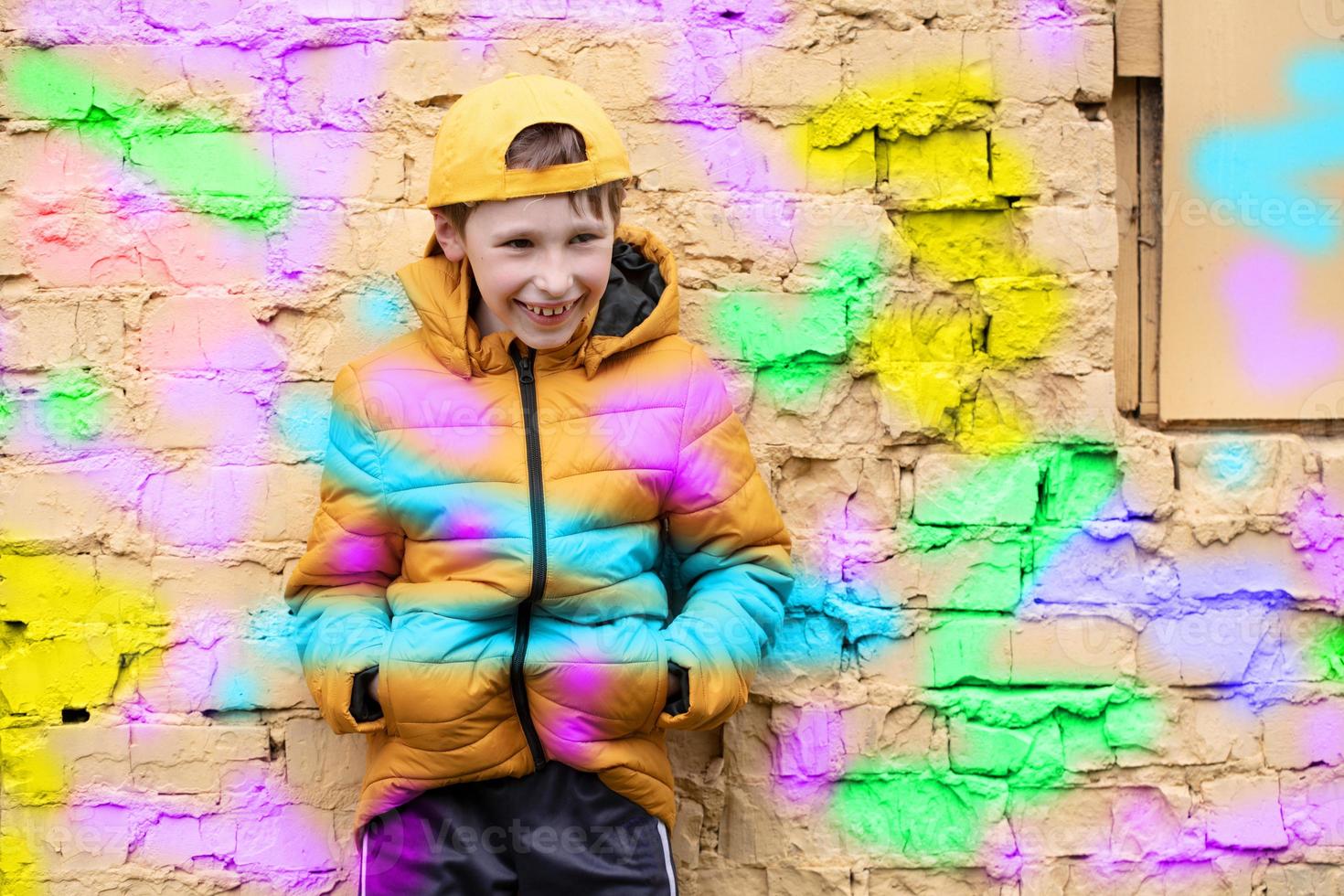 bambino nel graffiti. il ragazzo è in piedi contro un' mattone parete nel alla moda Abiti e un' baseball berretto, delineato con luminosa colori. foto