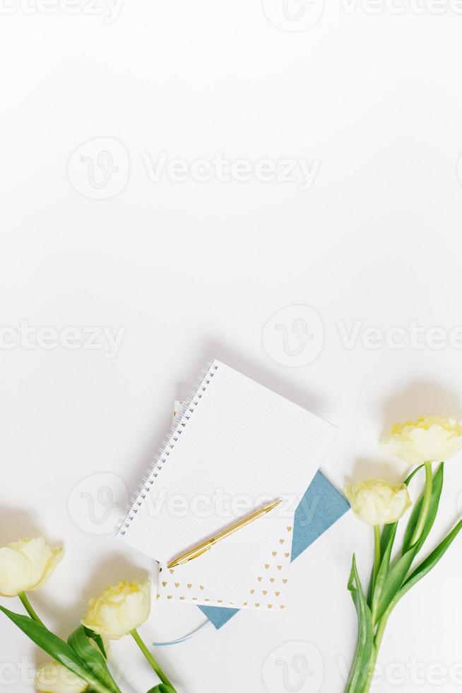 il di blogger primavera piatto posizione. bianca bloc notes, penna, mazzo di giallo tulipani su un' bianca sfondo con copia spazio foto