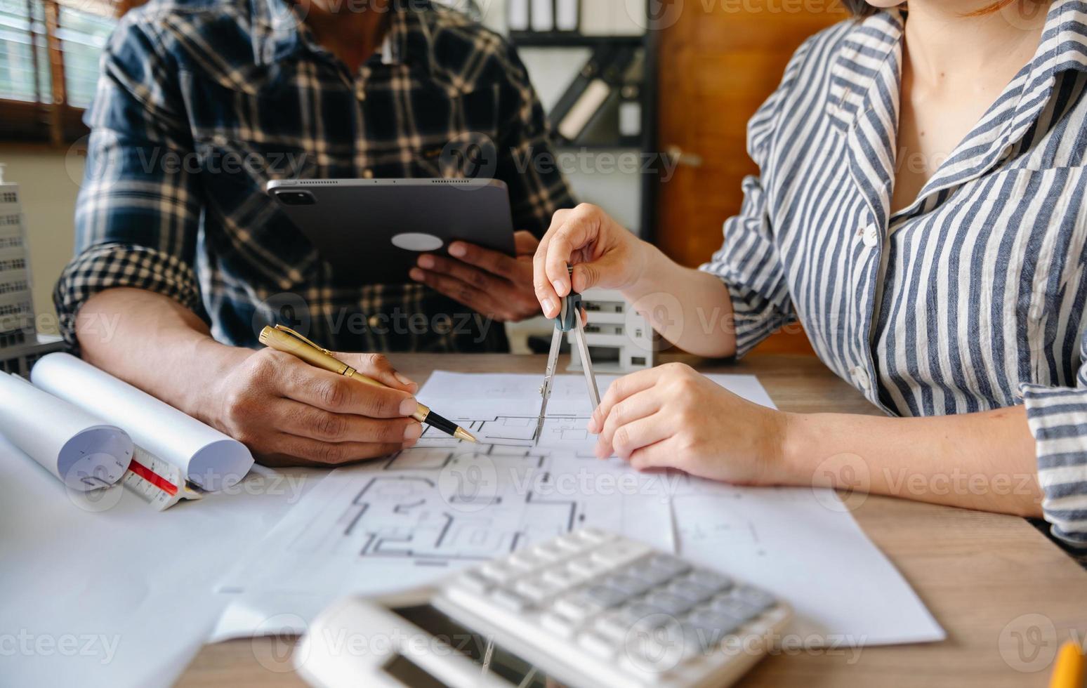 due colleghi che discutono di dati di lavoro e tablet, laptop con sul progetto architettonico in cantiere alla scrivania in ufficio foto