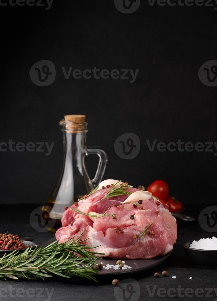 un' pezzo di Maiale prosciutto su un' nero tavola e spezie oliva olio, sale, rosmarino ramo e Pepe foto