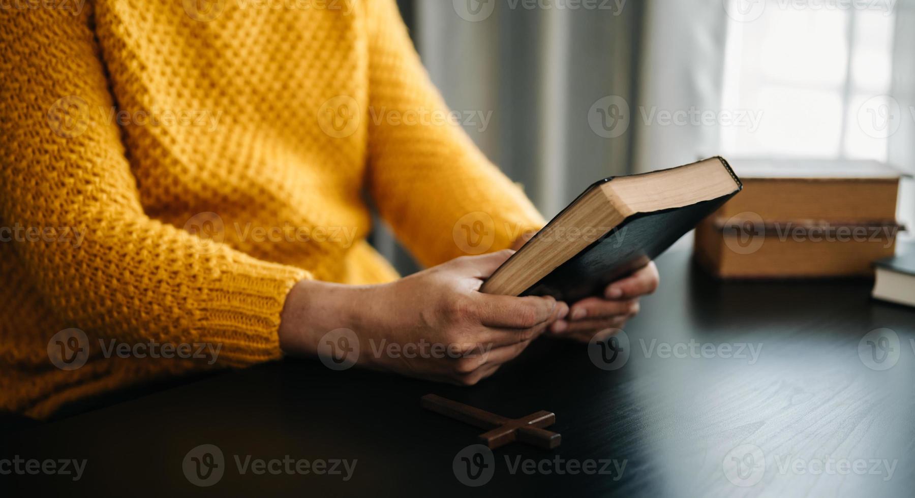 mani insieme in preghiera a Dio insieme alla Bibbia nel concetto cristiano e nella religione, la donna prega nella Bibbia sul tavolo di legno foto