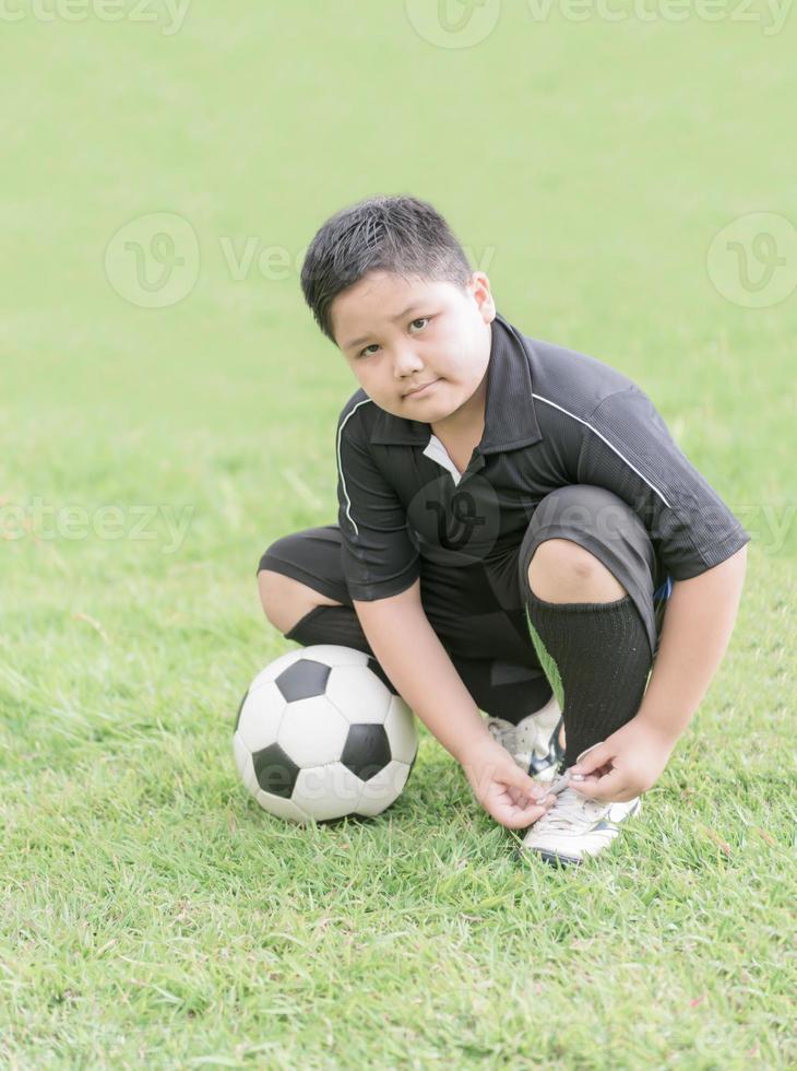 obeso ragazzo legatura il suo calcio scarpe, salutare concetto foto