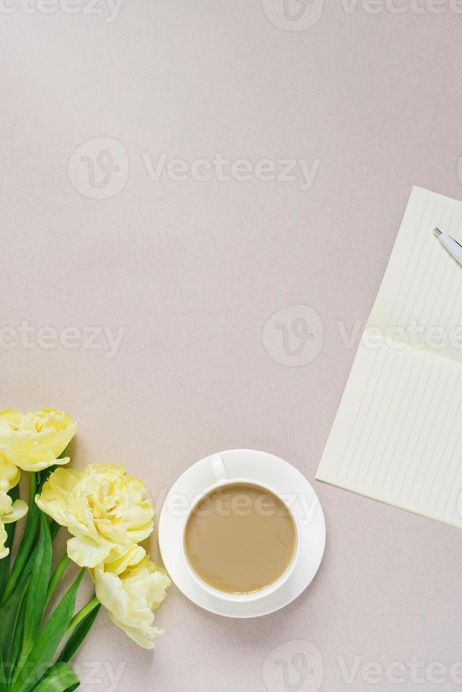 superiore Visualizza su il sfondo di un' del desktop con un' bloc notes e un' penna con un' tazza di caffè con latte. piatto posare giallo tulipano fiori piatto. del desktop copia spazio, spazio di lavoro, Stazionario. foto