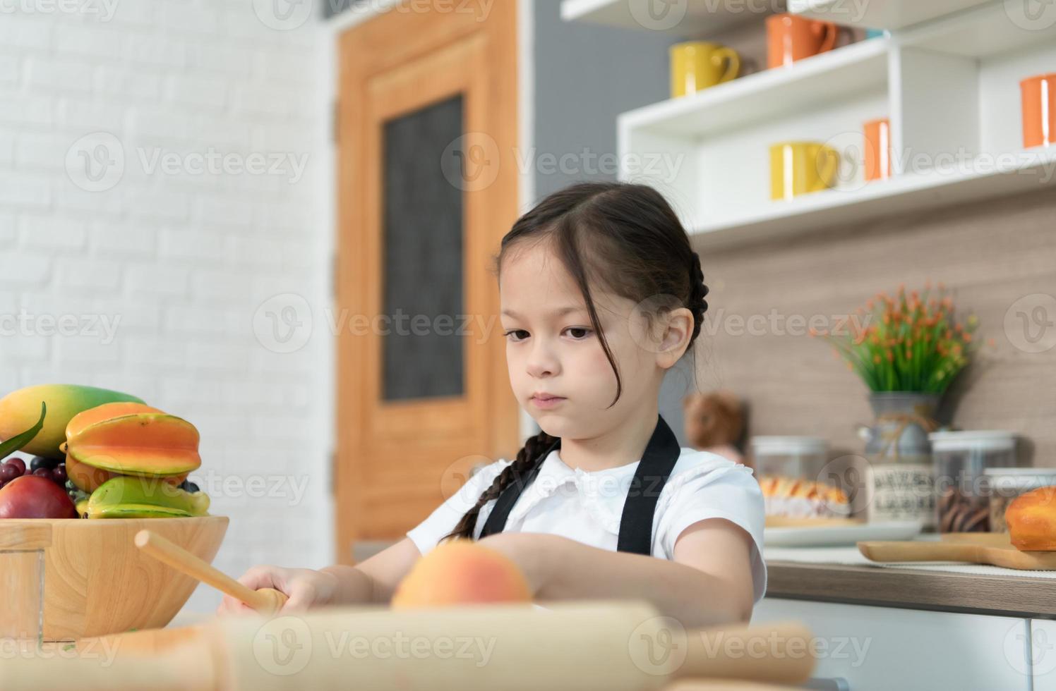 ritratto di un' poco ragazza nel il cucina di un' Casa avendo divertimento giocando con frutta giocattolo e utensili da cucina foto