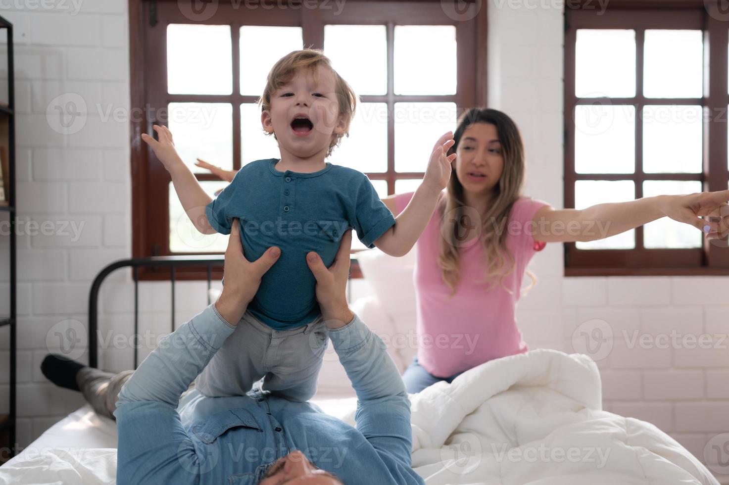 poco ragazzo volante con papà utilizzando il suo gambe per Aiuto lui volare alto via il pavimento di il suo letto nel il Camera da letto. foto