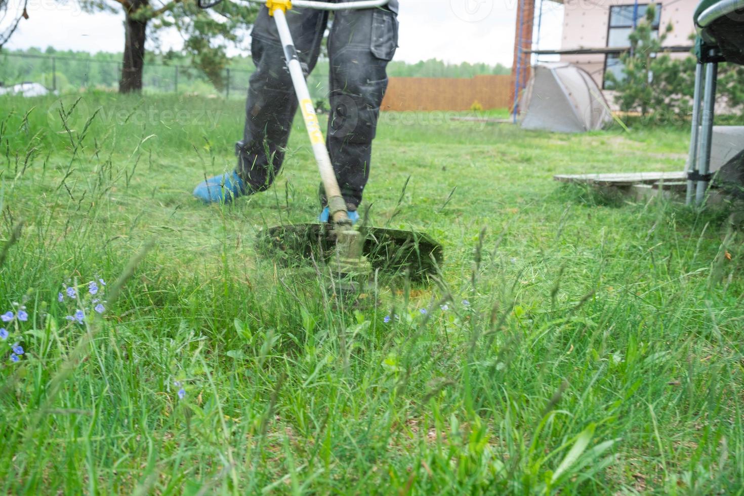 un' maschio giardiniere falcia il verde erba di il prato nel il Giardino dietro la casa con un' benzina tosaerba. trimmer per il cura di un' giardino tracciare foto