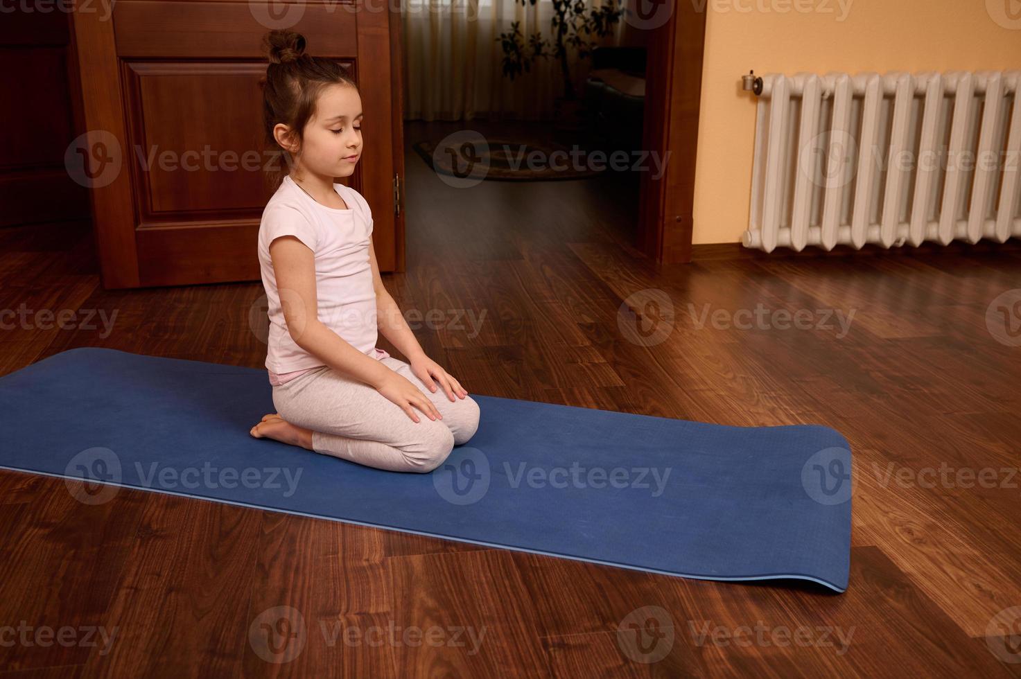 adorabile poco bambino ragazza medita con sua occhi chiuso su un' fitness stuoia durante yoga pratica foto