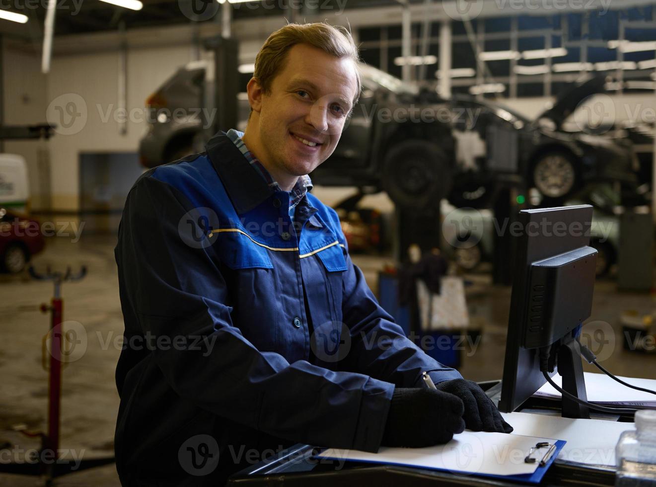 concentrato auto meccanico tecnico auto ingegnere sorrisi guardare a telecamera scrittura lista di controllo su appunti e Lavorando su tenere sotto controllo mentre manutenzione un' auto nel il auto servizio foto