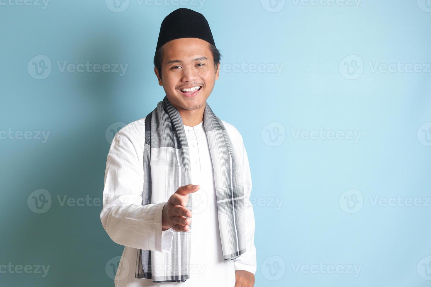 ritratto di attraente asiatico musulmano uomo nel bianca camicia raggiungendo su il suo mano per un' stretta di mano, accogliente qualcuno. isolato Immagine su blu sfondo foto