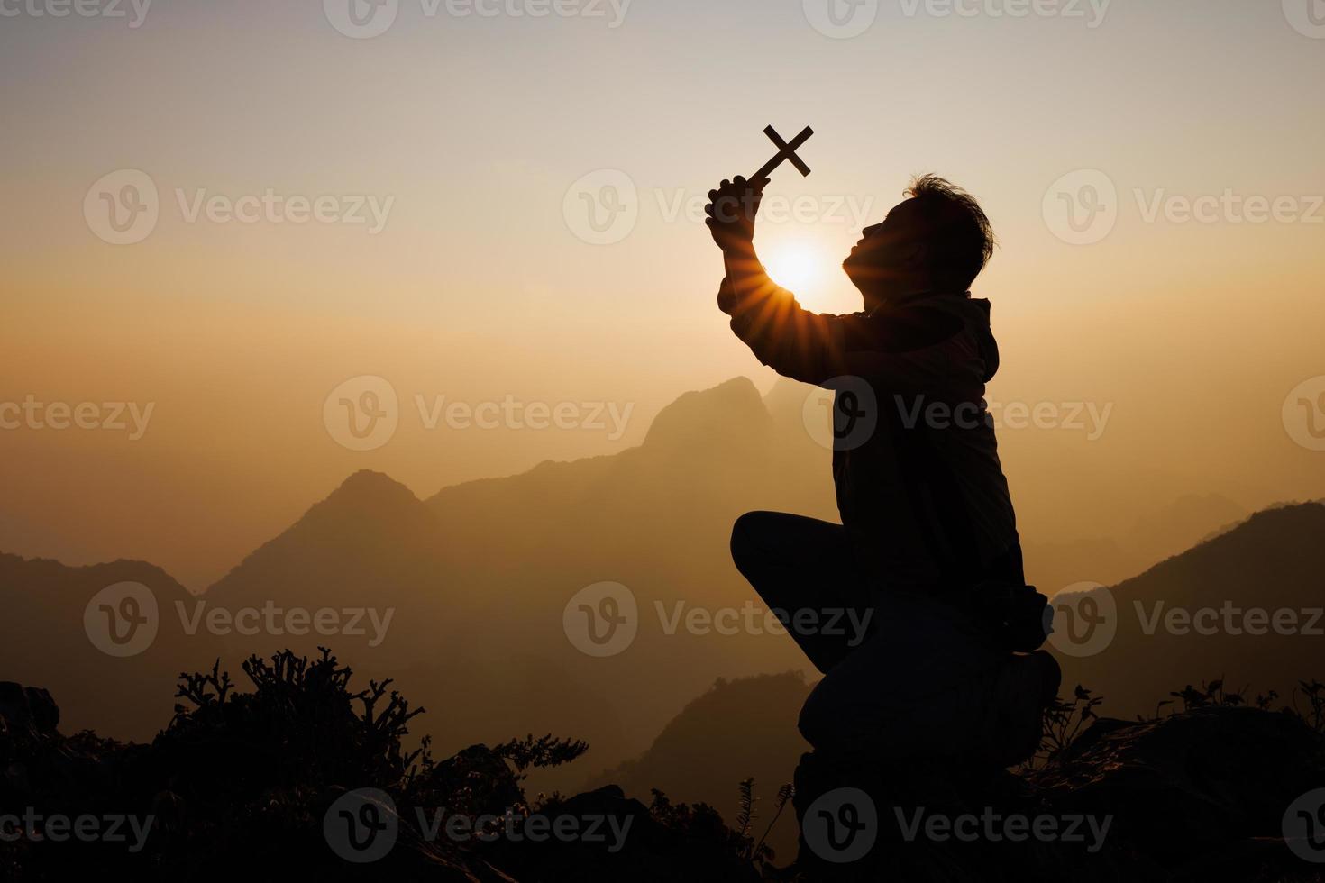 silhouette di un' uomo con un' crocifisso nel il suo mani preghiere per Dio. mentre il sole è crescente lode il religione. supremo fede nel il Dio di successo. avventura, viaggiare, religioso fede. foto