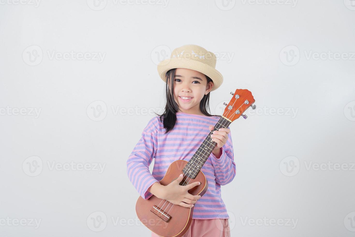 carino poco ragazza nel costume da bagno giocando ukulele. contento vacanza concetto. foto