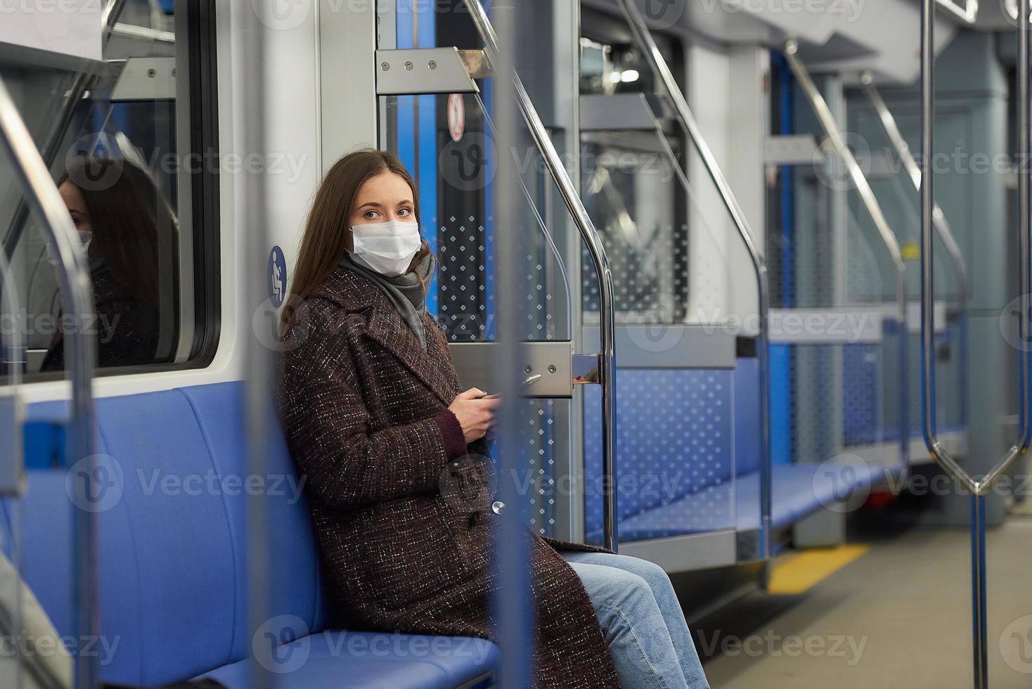 una donna con una maschera è seduta e utilizza uno smartphone in un moderno vagone della metropolitana foto