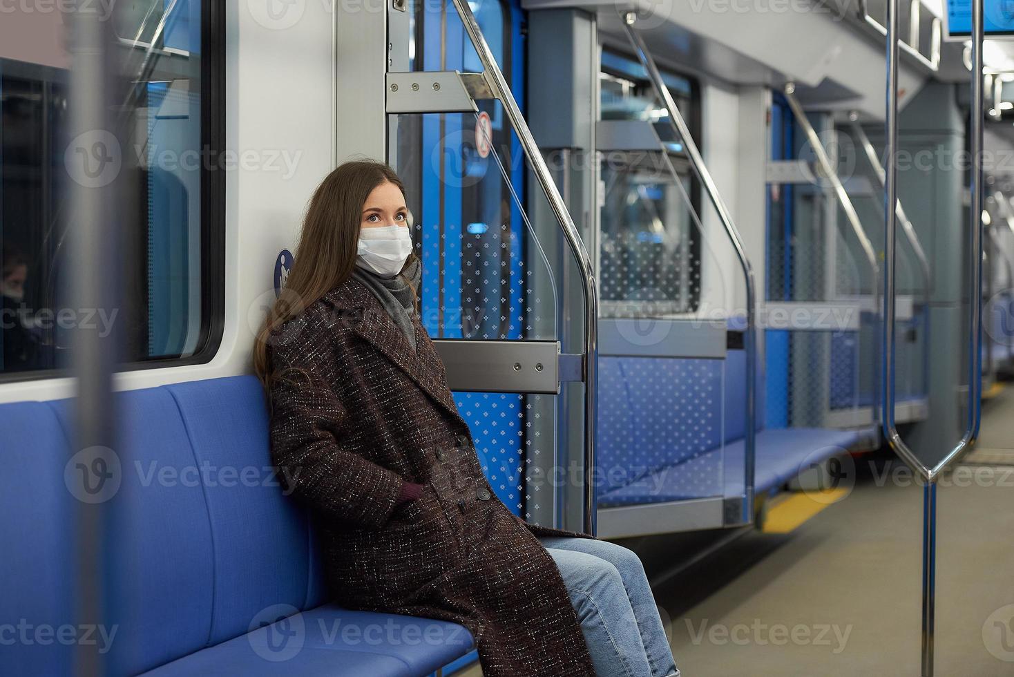 una donna con una maschera medica sta mantenendo le distanze sociali in un moderno vagone della metropolitana foto