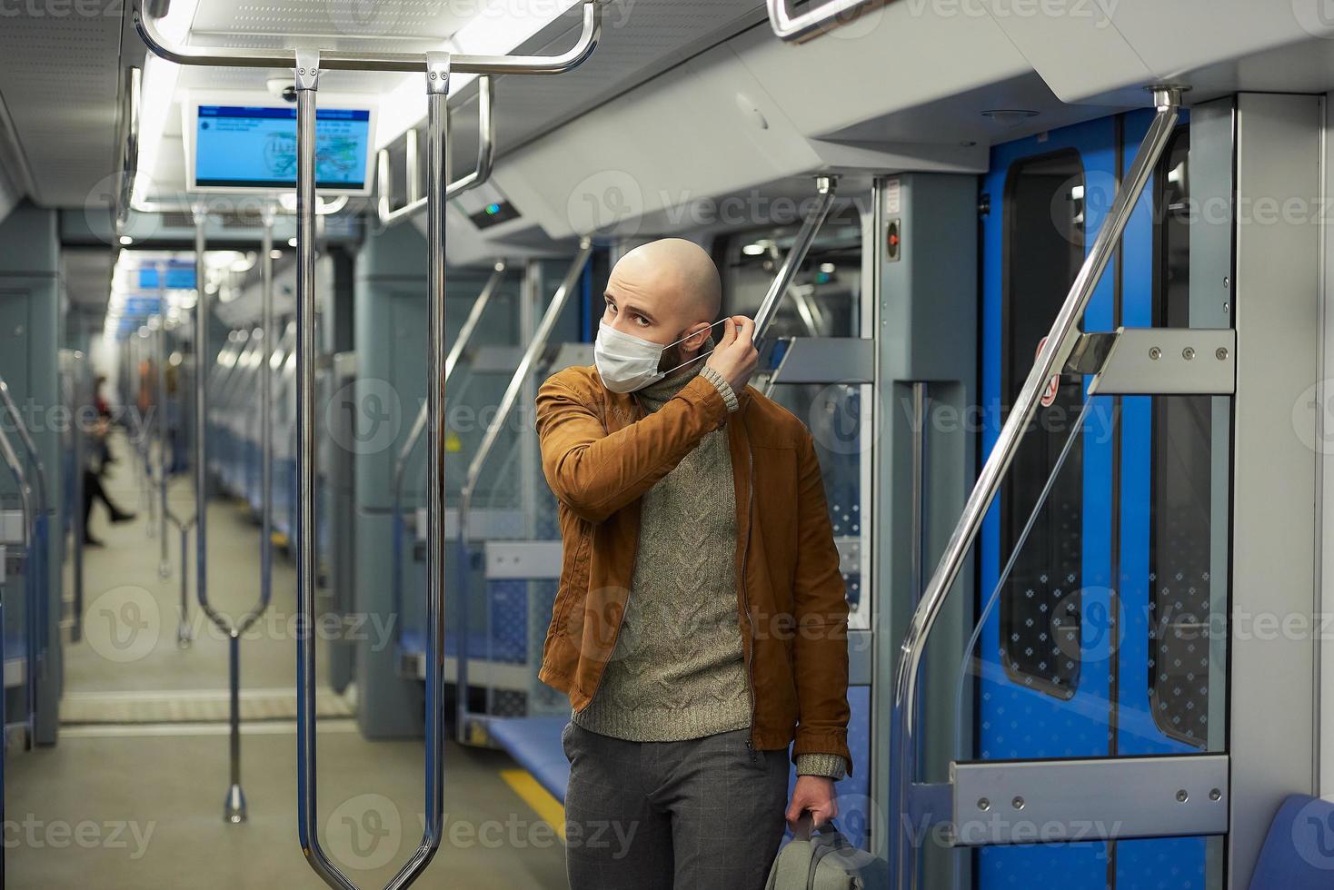 un uomo con la barba si sta mettendo una maschera medica in un vagone della metropolitana foto