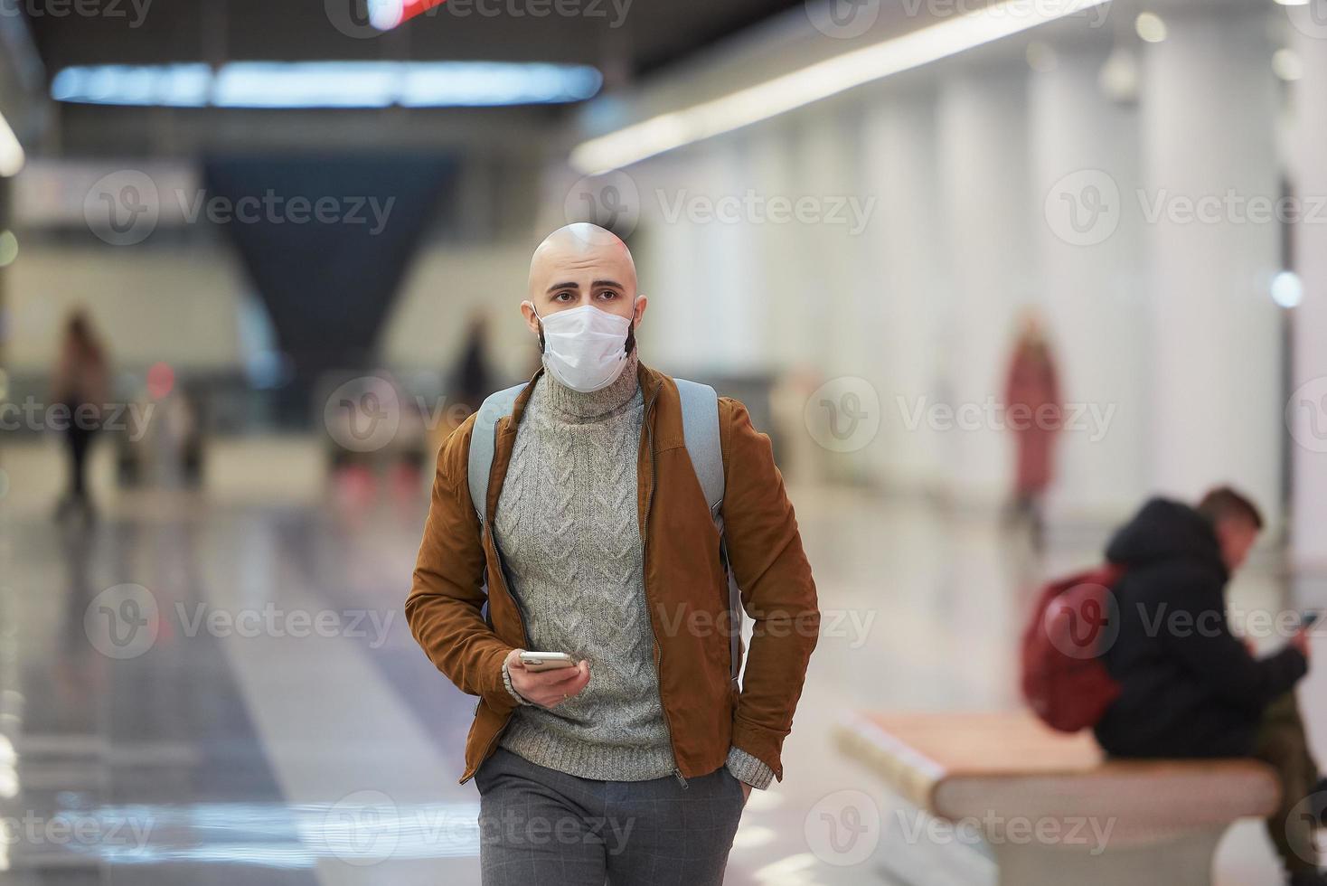 un uomo con una maschera facciale sta usando uno smartphone mentre aspetta un treno della metropolitana foto