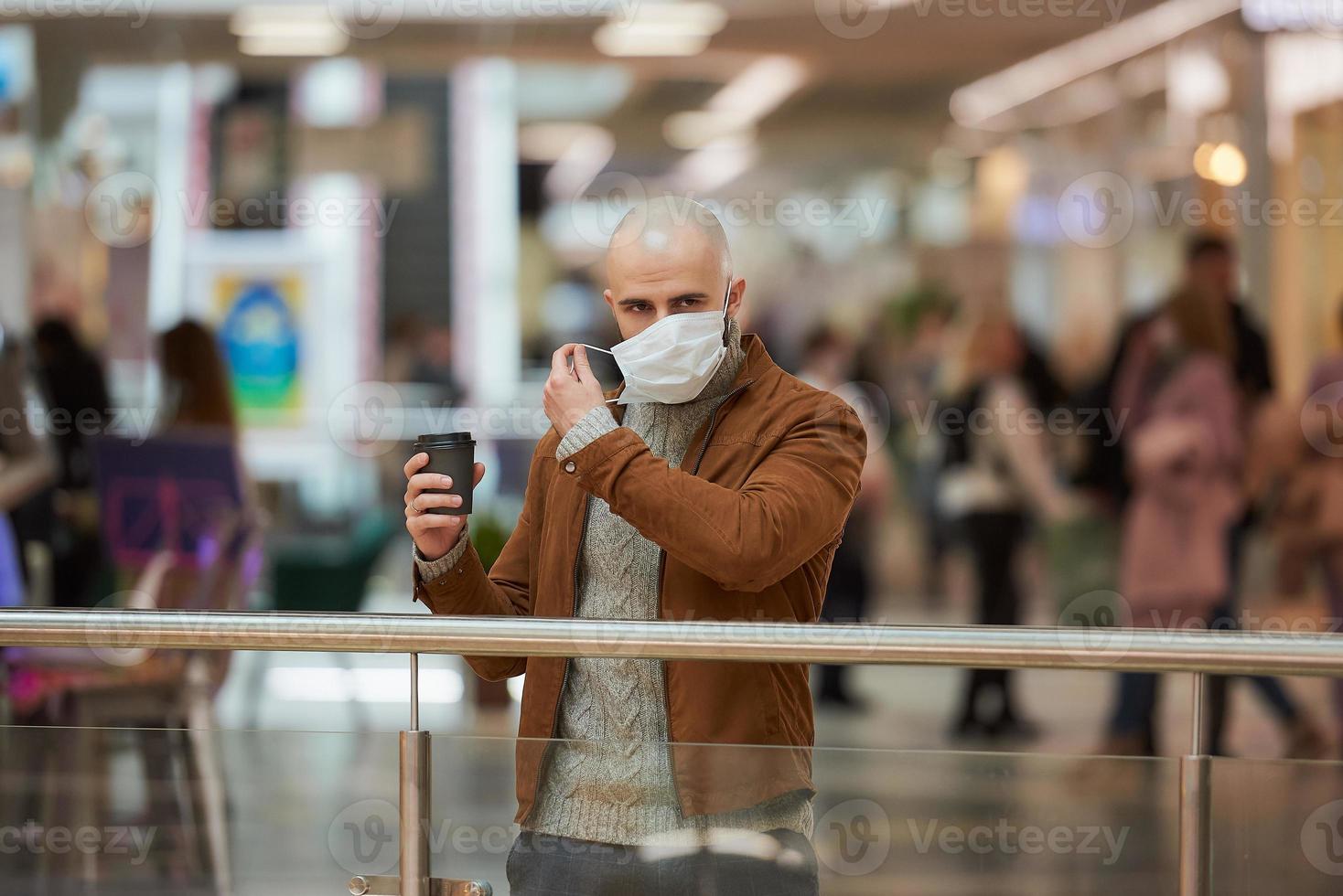 un uomo si sta mettendo una maschera mentre tiene una tazza di caffè nel centro commerciale foto