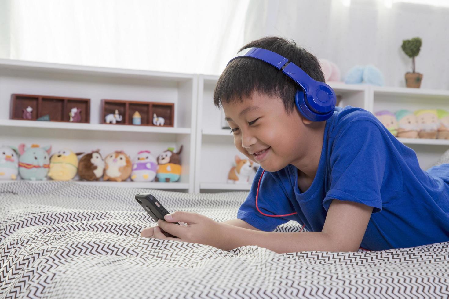giovane ragazzo asiatico in cuffie blu sorridendo e ascoltando musica a casa foto
