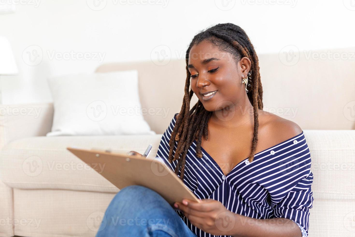 ritratto di bellissimo giovane africano donna Lavorando a casa. femmina seduta e scrittura Appunti. foto