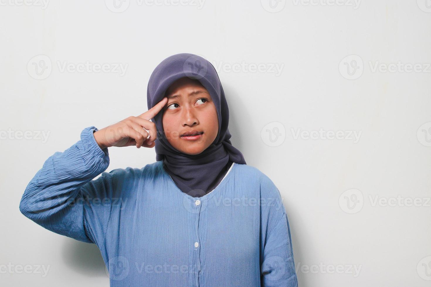 riflessivo giovane asiatico ragazza nel hijab è pensiero con sorridente viso foto