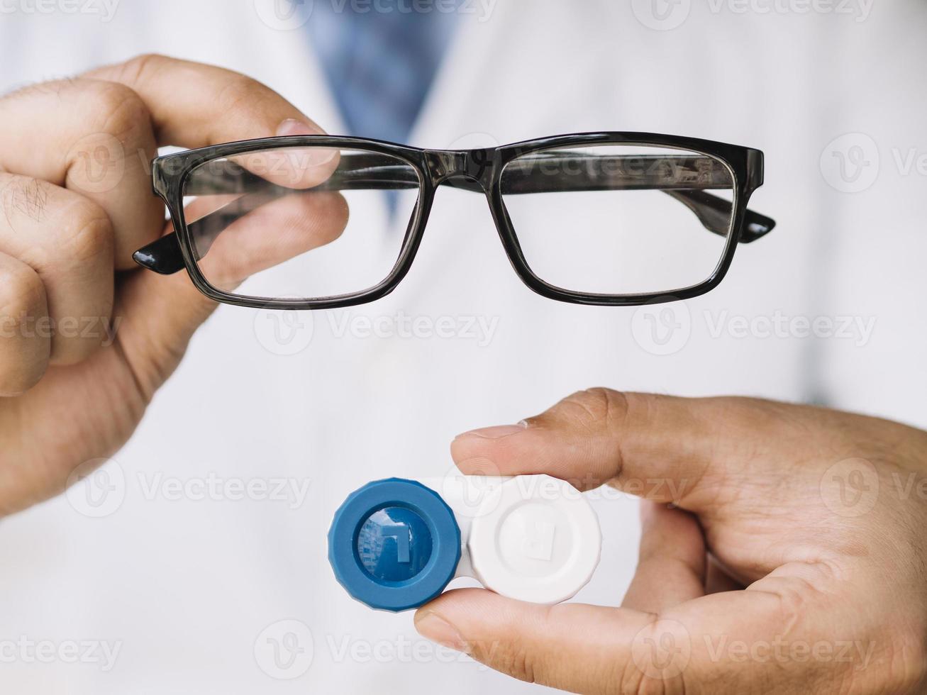 medico maschio che mostra un paio di occhiali neri e lenti a contatto foto