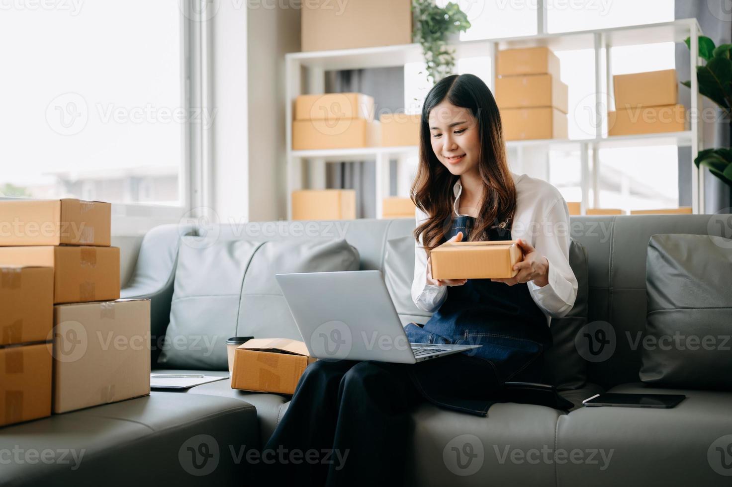 giovane asiatico attività commerciale proprietario donna preparare pacco scatola e in piedi dai un'occhiata in linea ordini per consegnare per cliente su tavoletta, il computer portatile shopping in linea concetto. foto