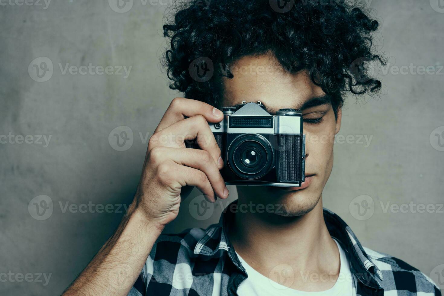 bello tipo con un' telecamera vicino il suo viso e Riccio capelli plaid camicia passatempo fotografo foto