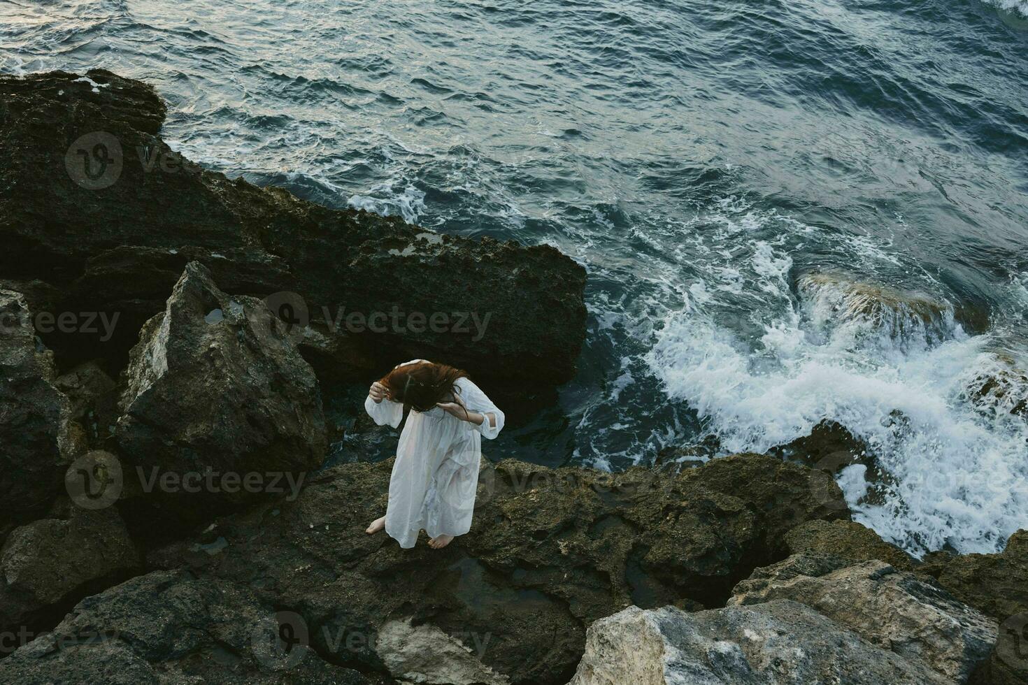 bella donna con bagnato capelli sta su il rocce di il oceano nuvoloso tempo metereologico foto