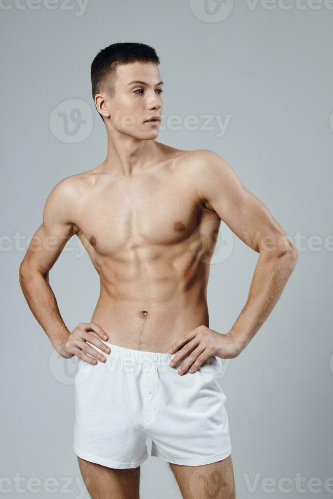 muscolare uomo con un' pompato su corpo Tenere il suo mani su il suo cintura bianca pantaloncini ritagliata Visualizza foto