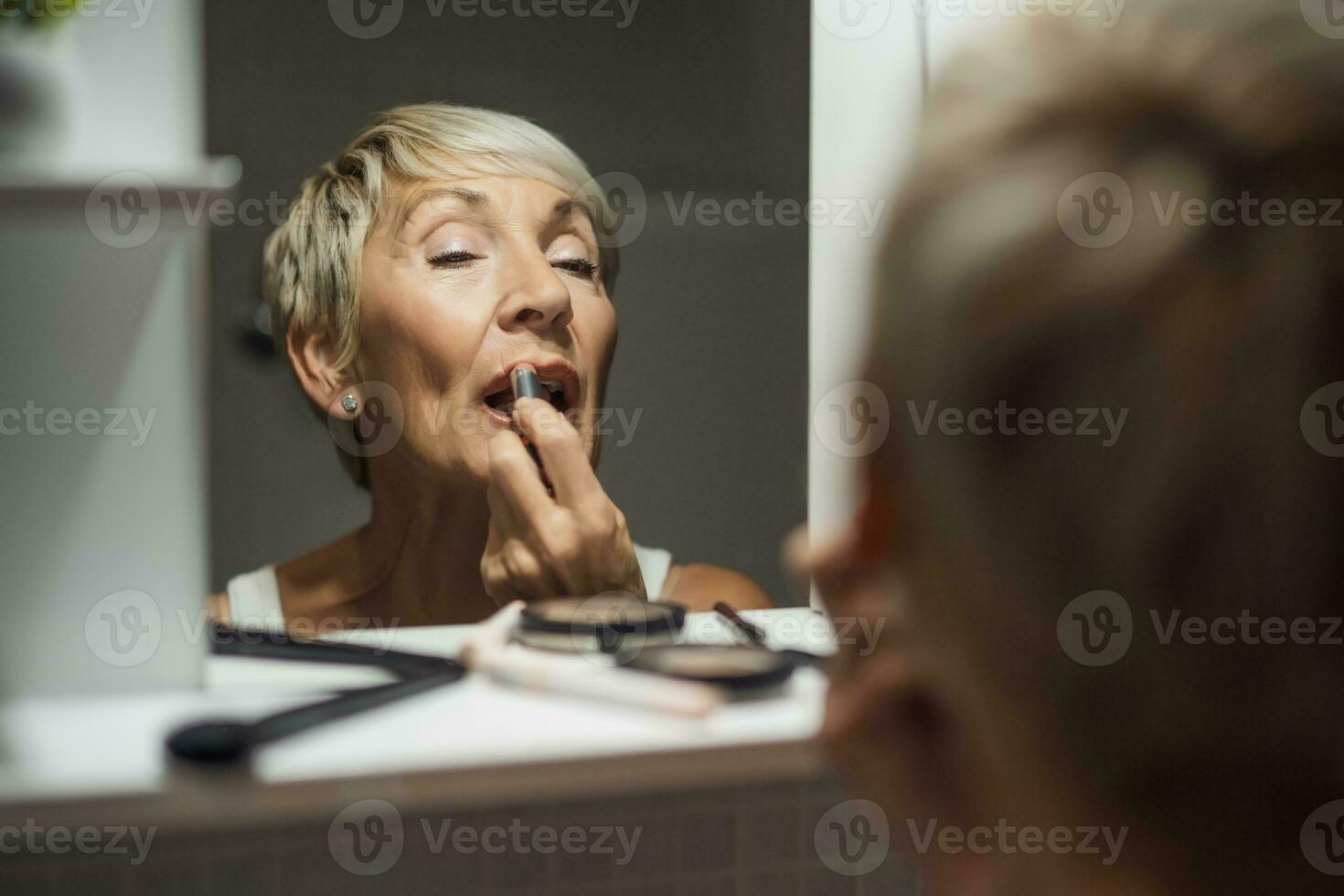 bellissimo maturo donna è l'applicazione trucco nel il bagno. foto