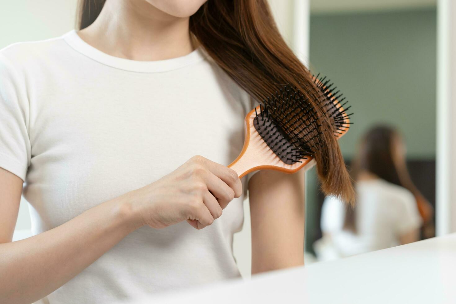 Salute capelli cura, bellezza trucco asiatico donna mano nel Tenere spazzola per capelli e spazzolatura, pettinatura sua lungo dritto capelli riflessione nel specchio nel mattina routine dopo salone trattamento a casa, acconciatura. foto