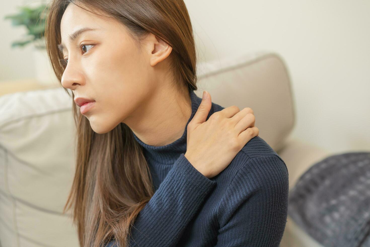 corpo muscoli rigido problema, asiatico giovane attraente donna, ragazza dolore con indietro dolore dolore a partire dal opera, Tenere massaggio sfregamento spalla male o irritato, doloroso seduta su divano a casa. assistenza sanitaria le persone. foto