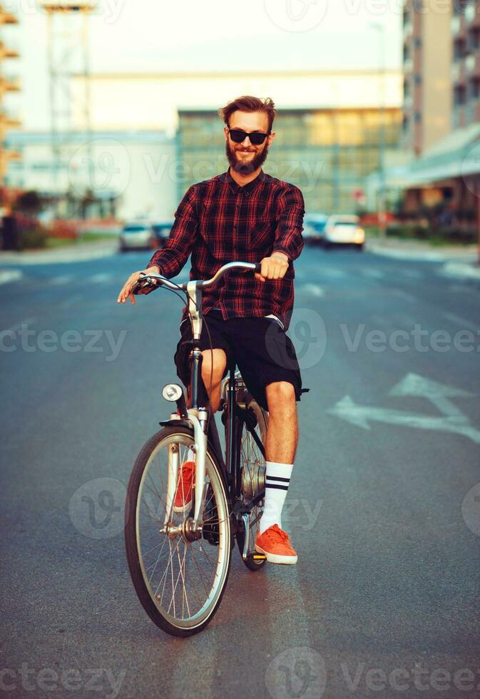 elegante uomo nel occhiali da sole equitazione un' bicicletta su città strada foto